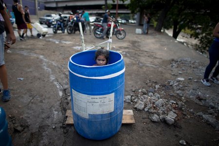 A little girl stands inside a plastic barrel while her family waits to collect water from an open pipe above the Guaire River, during rolling blackouts which affect the water pumps in people's homes, offices and stores, in Caracas, Venezuela.<br/>(Ariana Cubillos/AP/Shutterstock)