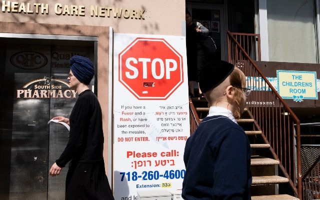 People walk past a sign outside of health clinic with warnings about measles in the Orthodox Jewish area of the Williamsburg neighborhood in Brooklyn, New York.